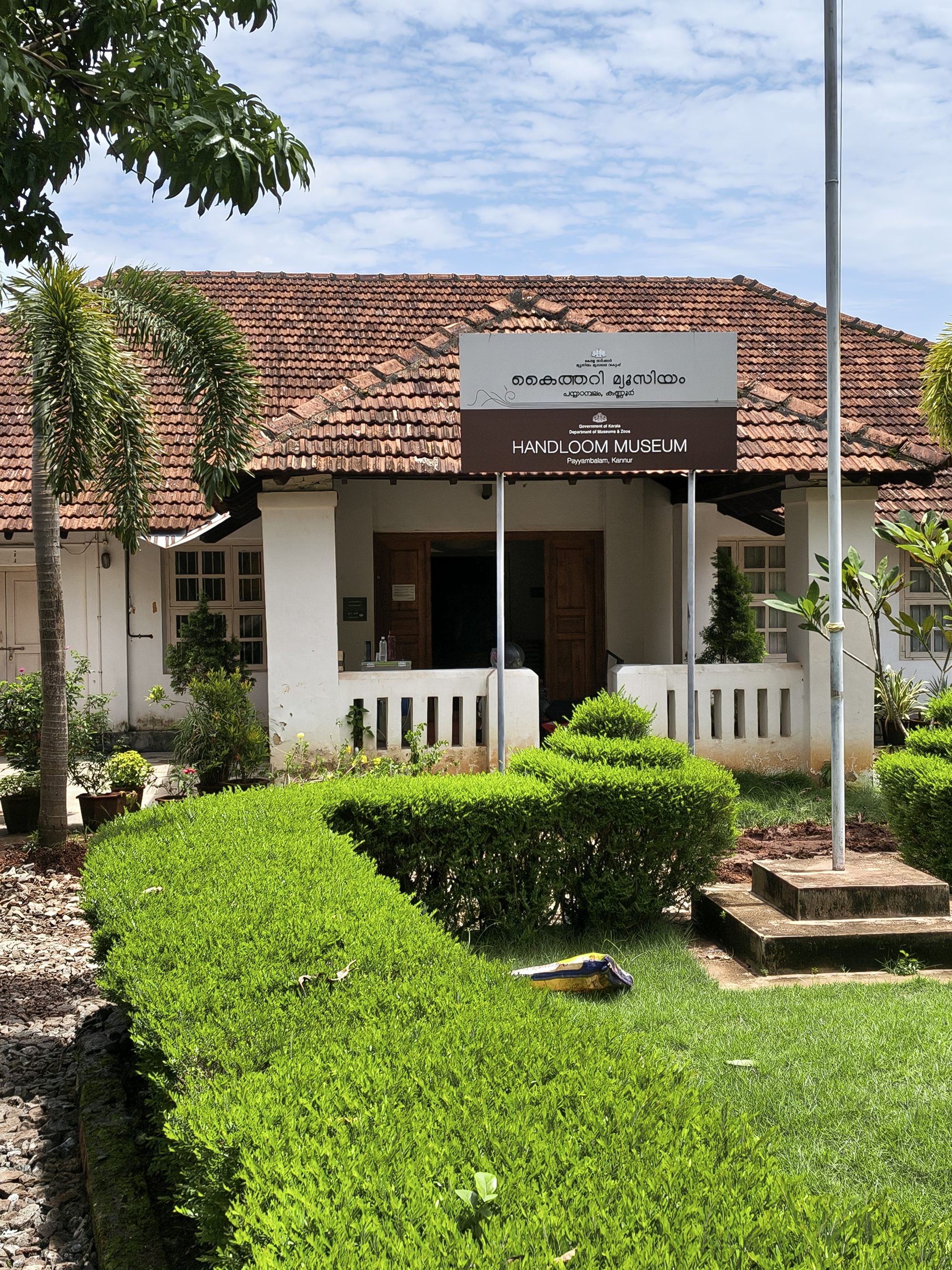 The Handloom Museum at Payyambalam, Kannur, a red-tiled building behind clipped green hedges