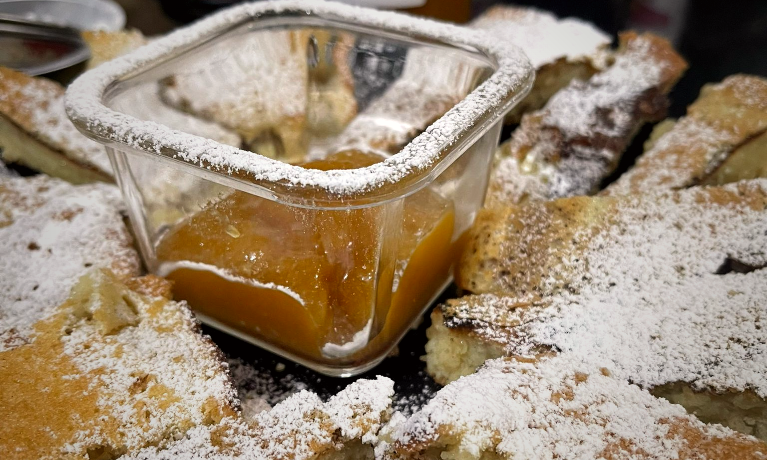 Home-baked bread dusted with sugar arranged around a glass dish of apricot jam