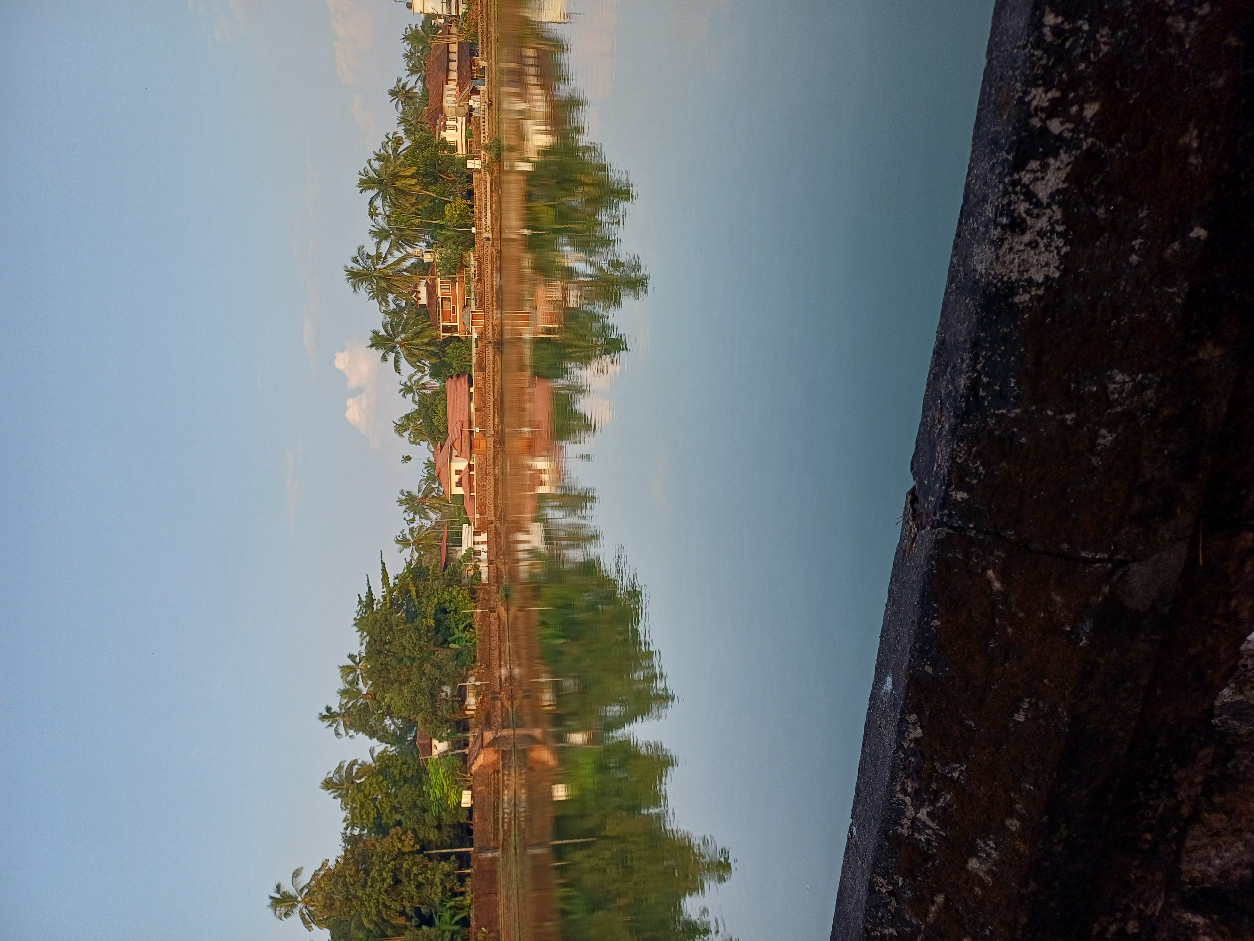 The temple pond at Kannur catching first light, palms and tiled houses reflected in still water